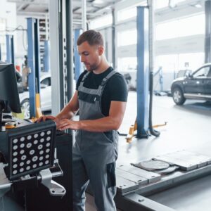 Looks at keyboard. Man at the workshop in uniform use computer for his job for fixing broken car