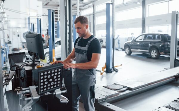 Looks at keyboard. Man at the workshop in uniform use computer for his job for fixing broken car