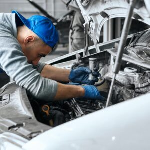 Mechanic in blue overalls checking serviceability of car engine