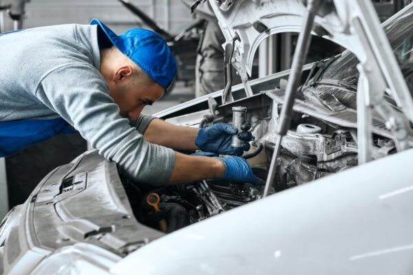 Mechanic in blue overalls checking serviceability of car engine