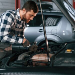 Repairing the electronics of the car under the hood. Man in uniform is working in the auto salon